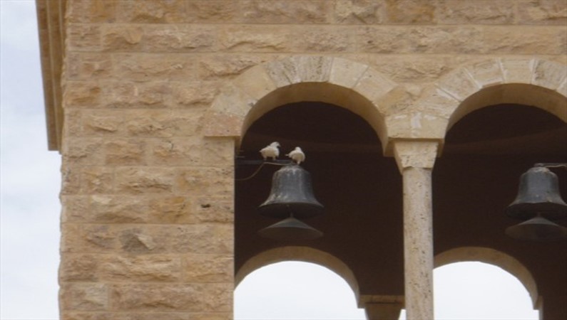 Колокольня греческой православной церкви Иоанна Крестителя. Белых голубей держит молодой священник